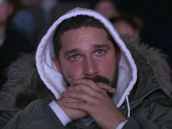 Homem branco de capuz com as mãos na altura da boca e os olhos cheios de lágrimas 