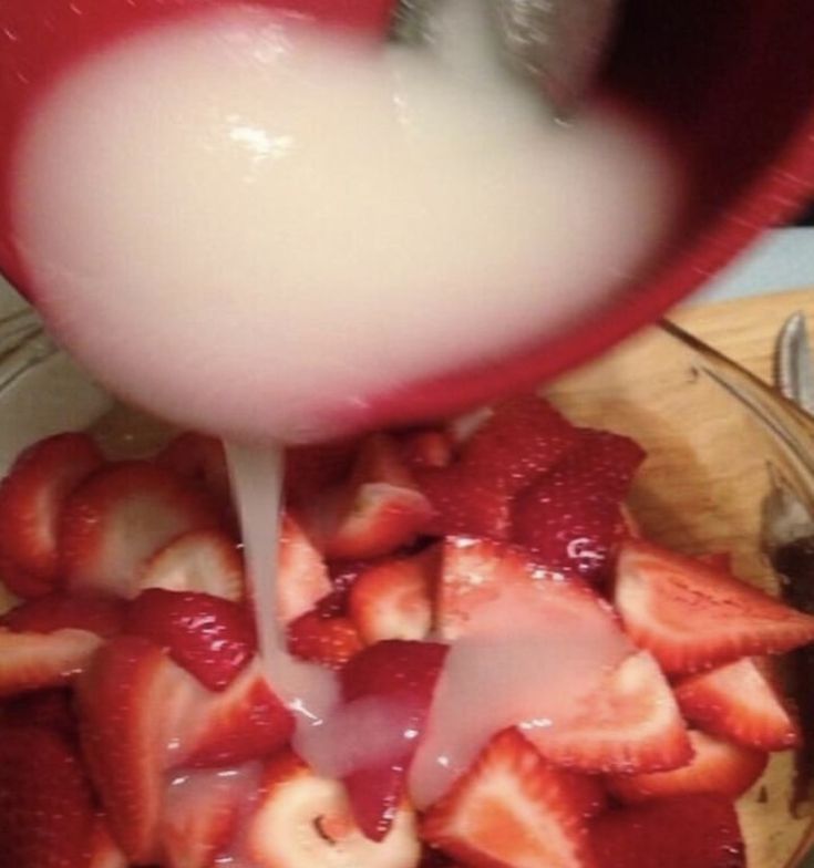 Morangos cortados e uma calda branca caindo em cima, parece gozo 