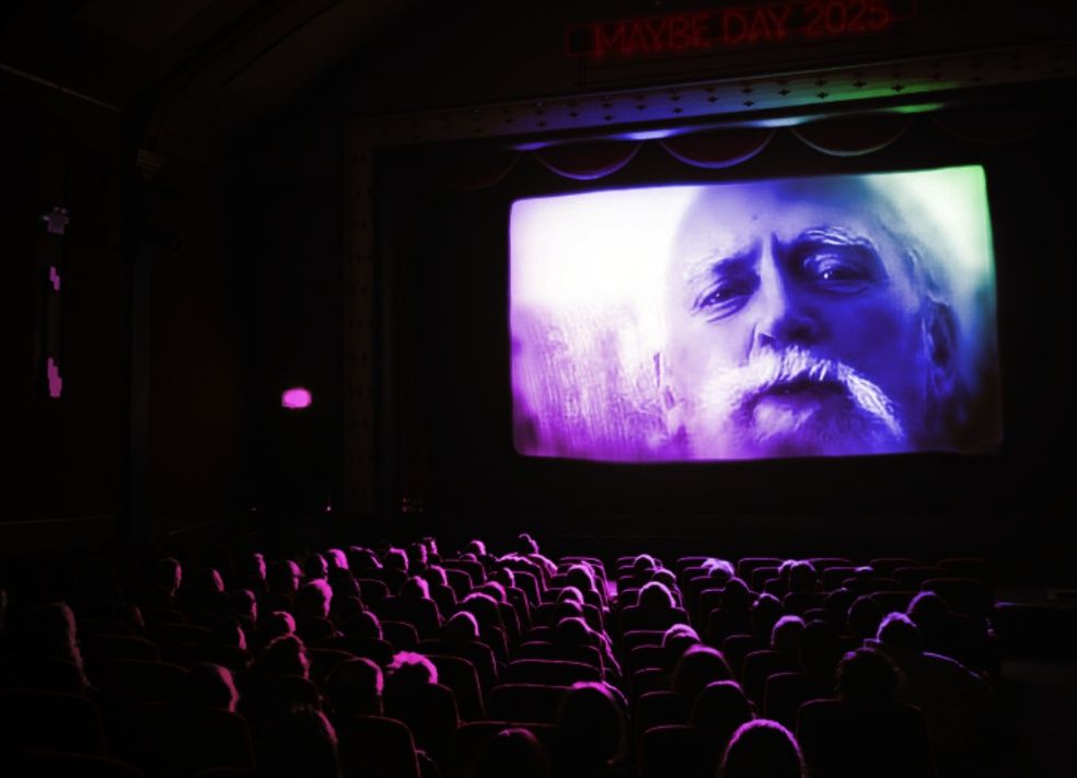 Colorful image of Robert Anton Wilson in a film screening, to mark Maybe Day 2025.