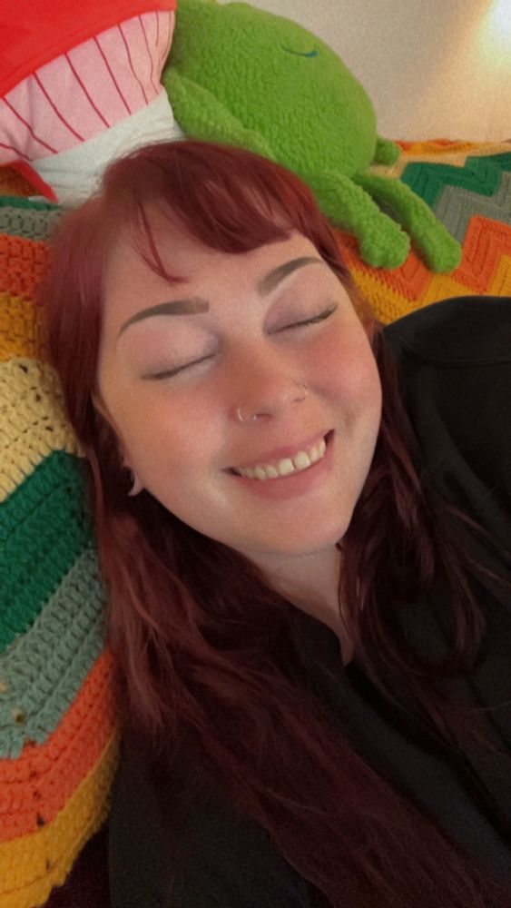 a picture of me, rattgirrll, laid back on the couch with my eyes closed and a big smile on my face. There is a mushroom and frog pillow above my head. 