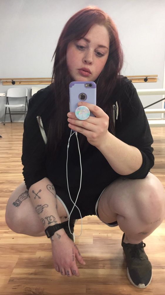 a photo of me in a mirror posing squatted wearing all black and holding a old iPhone up. 