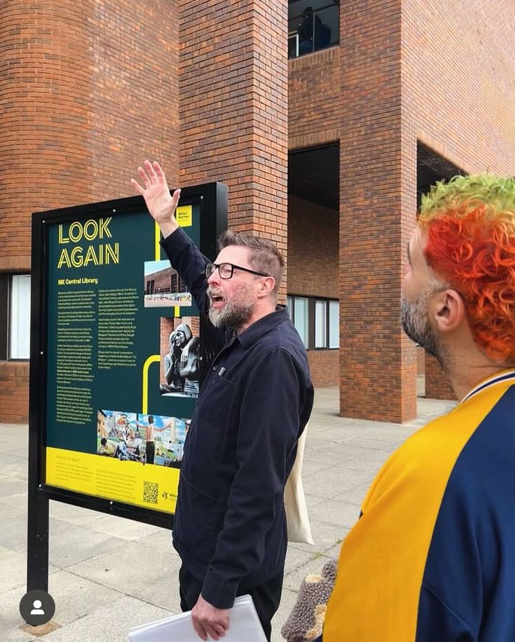 A man waving his hands theatrically in front of Milton Keynes Library 