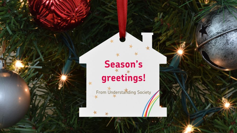 A house-shaped christmas bauble hanging on a christmas tree.