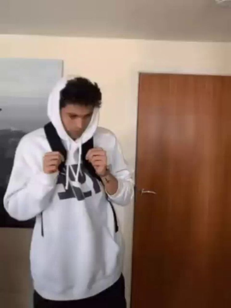 a man wearing a white hoodie and a backpack is standing in a room .