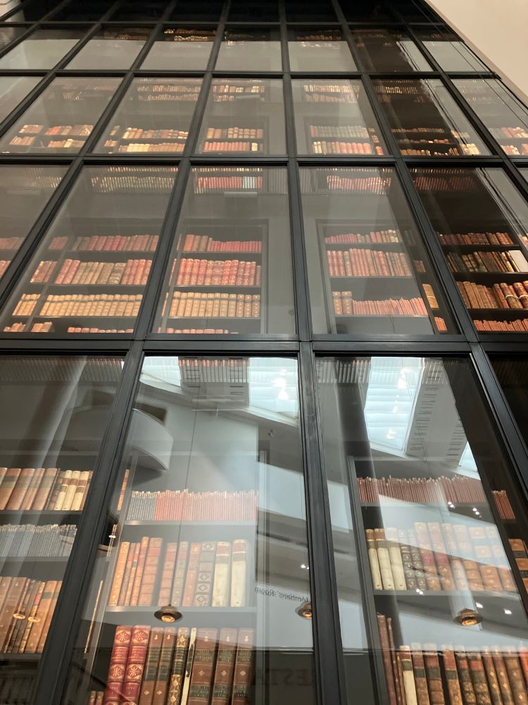 Image of the library of King George III inside The British Library. Shelves of old books behind glass tower upwards like a skyscraper viewed from its base. 