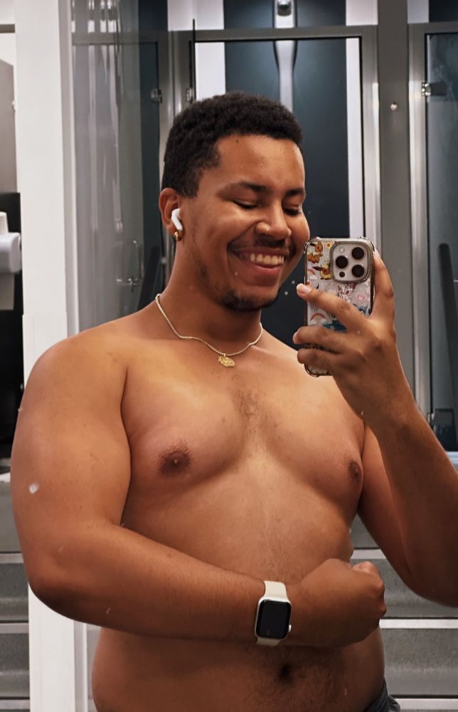 a shirtless mirror selfie of joel, who’s flexing their left arm 