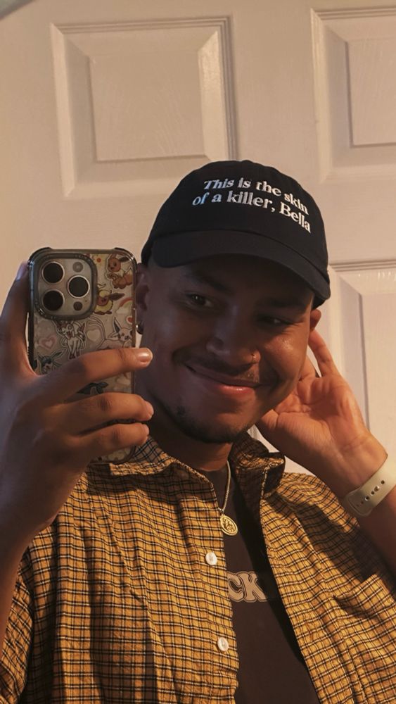 a mirror selfie of joel wearing a navy cap that says “this is the skin of a killer, bella” 