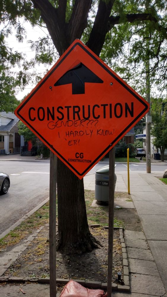 Photo of an orange "Construction ahead" sign. Someone has written "Gender? I hardly know 'er!" on the lower half.