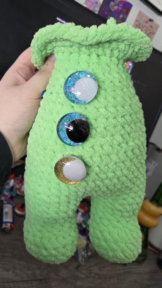 the start of a green crocheted alien. i have places 3 different eyes in his body to figure out which color i like best!