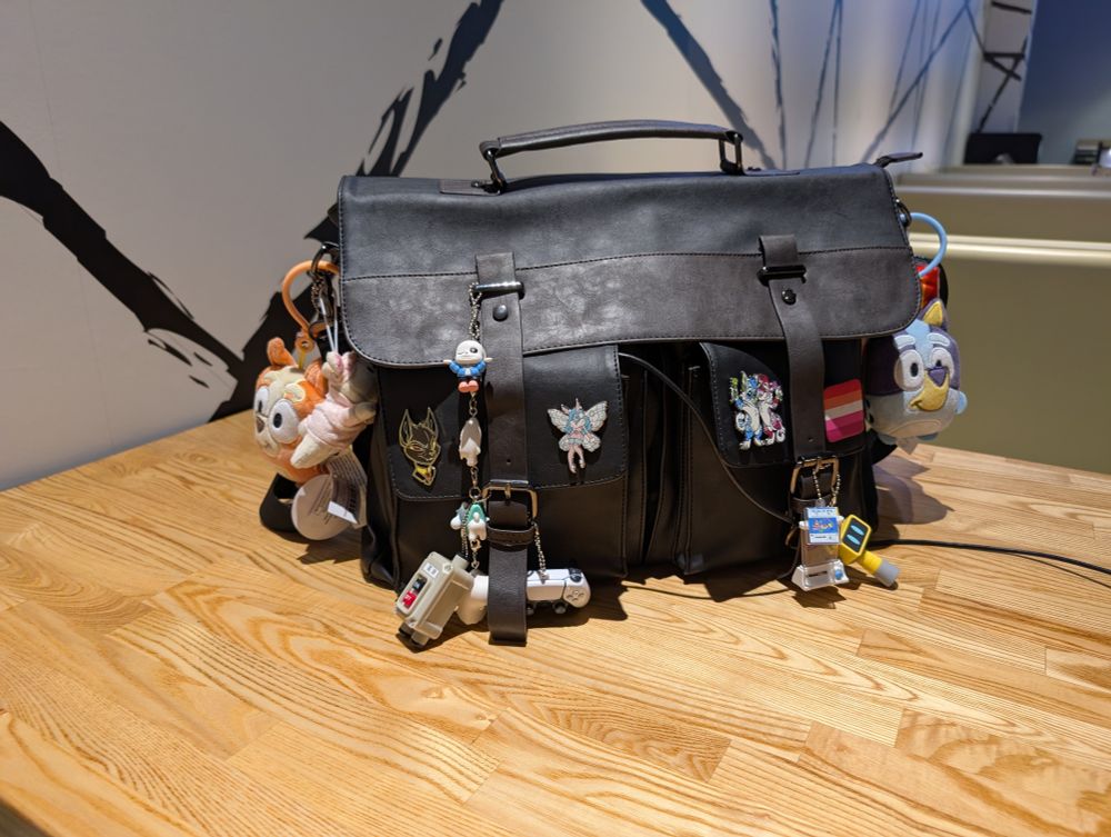 A large black leather bag with a copious amount of keychains, pins, and hanging objects on it. 