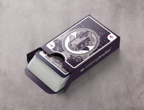A stylized deck of playing cards in a navy blue box with the Training Tracker logo and name. The deck's box features a dark circular emblem with a technical grid pattern background. A few cards are fanned out showing similar geometric designs in navy and white. The cards appear to have a modern, technical aesthetic matching aviation themes.