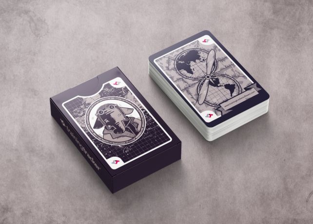 Training Tracker playing cards on a gray background. On the left, a navy blue card box showing the elephant mascot design. On the right, a fanned-out deck showing the card backs with a world map and propeller design. The Training Tracker logo and website appear in small text on the cards.