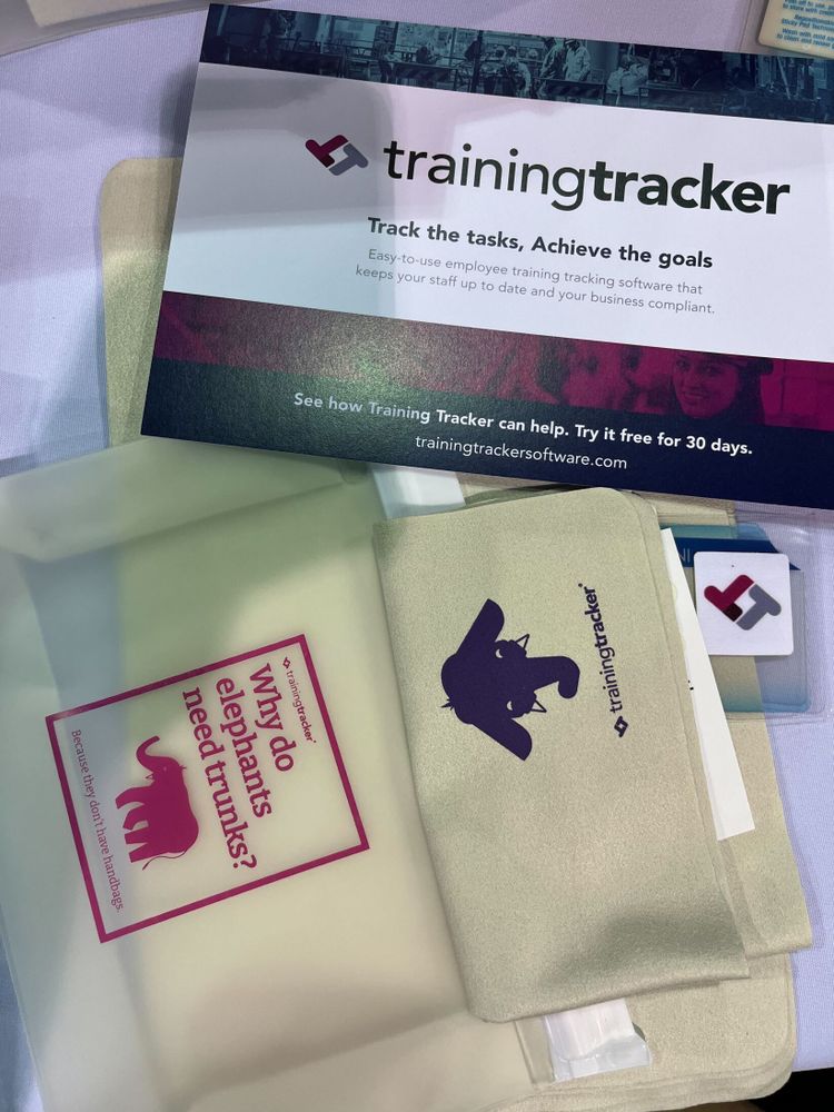 Training Tracker promotional materials including a flyer with their logo and tagline "Track the tasks, Achieve the goals" describing employee training software. Below are branded swag featuring the Training Tracker elephant asking "Why do elephants need trunks?" The materials showcase the brand's pink, purple and gray color scheme.
