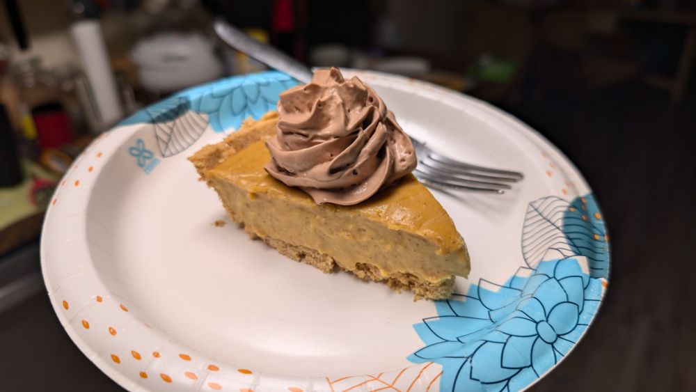 A slice of butterscotch cinnamon pie with a dollop of chocolate whipped cream sits on a paper plate, ready to be eagerly devoured.