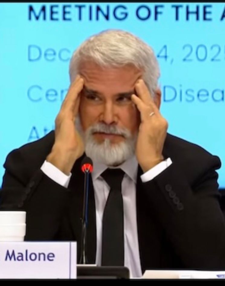 Robert Malone cups his hands on either side of his face, pushing his forehead up into creases, while looking to his right (mouth closed).