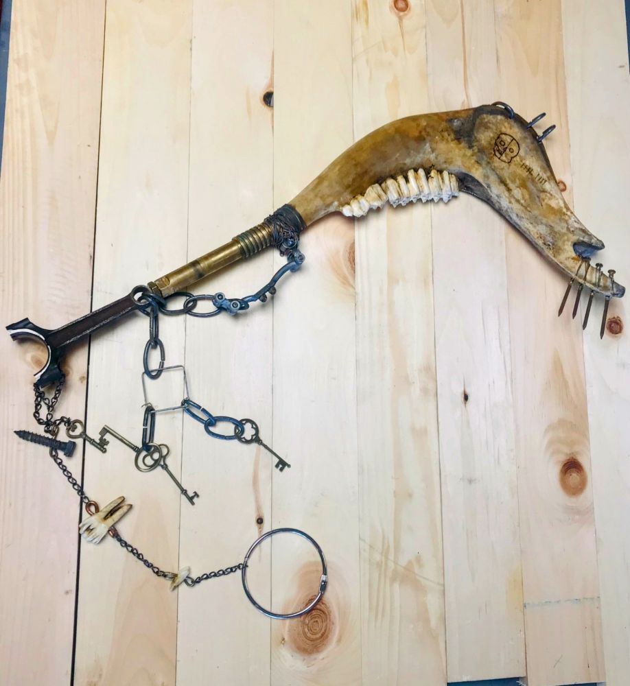 A jawbone cudgel with a brass grip and nails attached to the end, it has a piston pommel and is adorned with chains lined with keys and teeth and other rusty hardware 