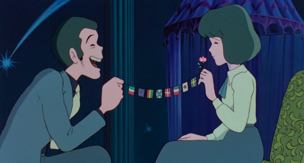 A handsome man and a young woman, a pink flower and a string of world flags between them. They are laughing.