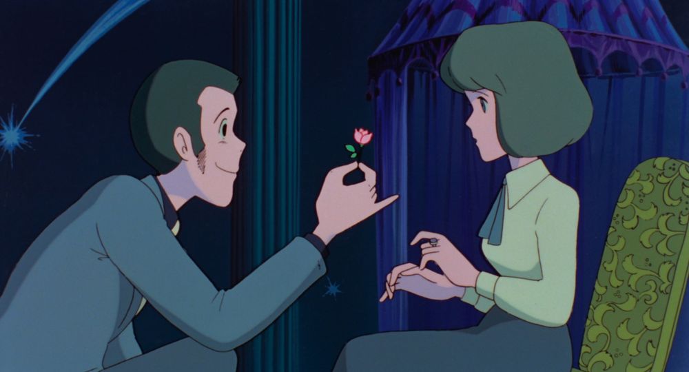 A handsome man holding out a small pink flower to a young woman.