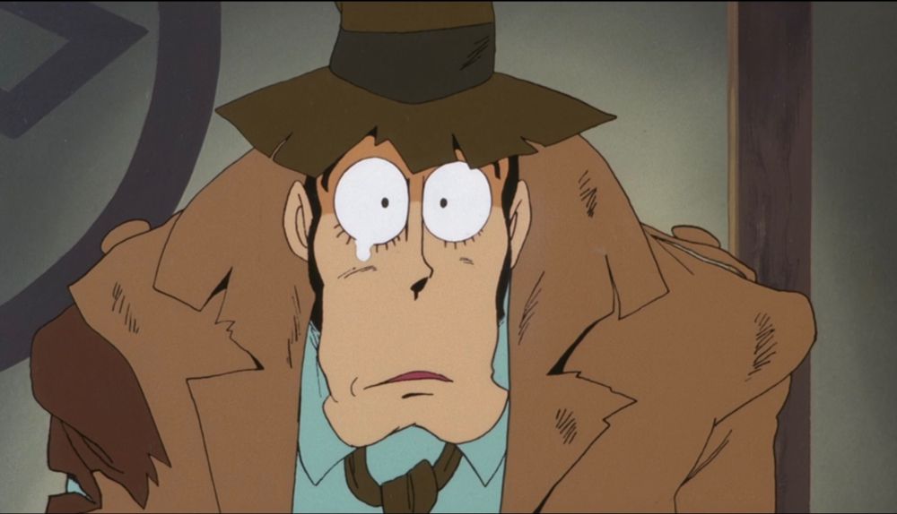 A man with a prominent chin and torn trenchcoat, looking stunned, with a tear in his eye