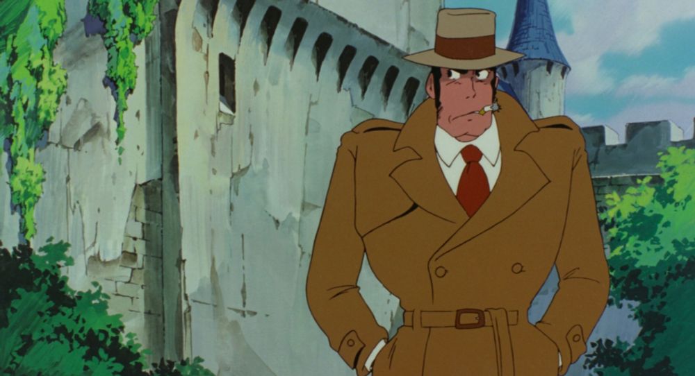 A man with a prominent chin smokes a cigarette while standing outside a castle. He looks disgruntled.