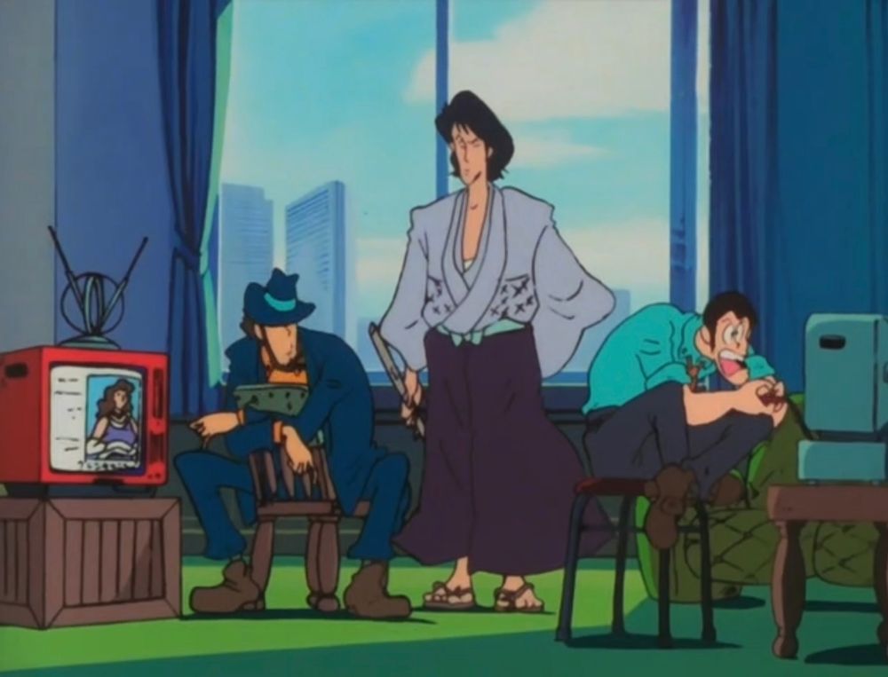 Three handsome men between two TVs. One is sitting Riker-style with his legs spread wide. One is standing and holding a sword. One is aggressively playing a video game.