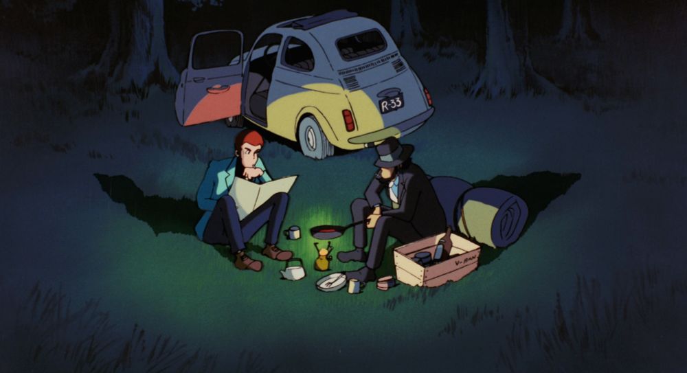 Two handsome men camping outside their Fiat 500. The one in the green jacket is reading a map. The one in the suit and hat is cooking food over a small gas fire.