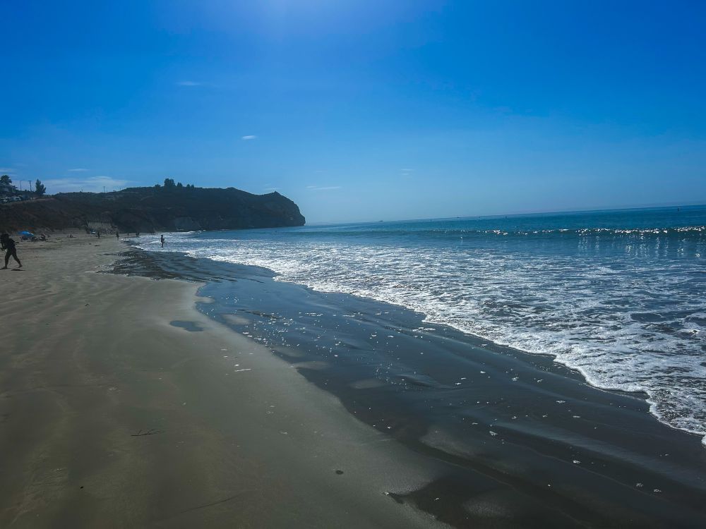 Waves breaking at Avila Beach with rugged mountain against a blue sky in the background 