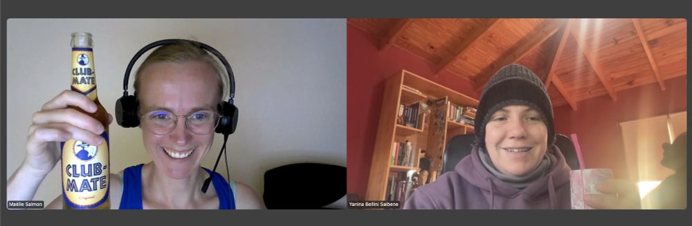 Screenshot from a Zoom call with Yani. She's wearing a sweater and a hat, and showing her hot mate. I am wearing a tank top and showing my cold Club Mate soda.