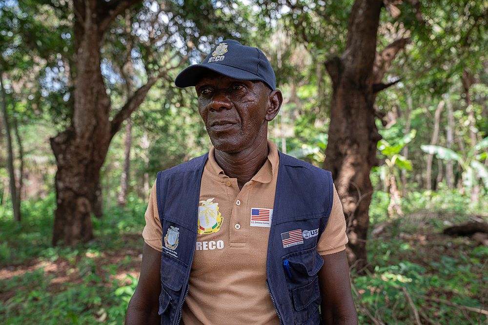 A middle-aged man wearing a vest with the American flag and the USAID logo on it.