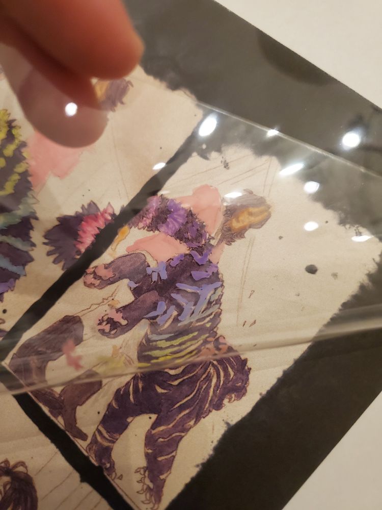 Lifting the transparent plastic film to show a printout of the black and white panel underneath.