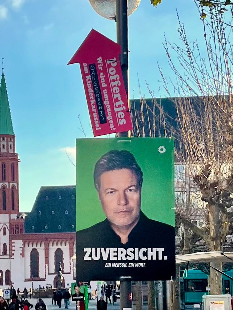 Ein Wahlplakat der Grünen zeigt Robert Habeck und das Wort Zuversicht in der Frankfurter Innenstadt. Direkt darüber: ein Schild für einen Poffertje-Stand.