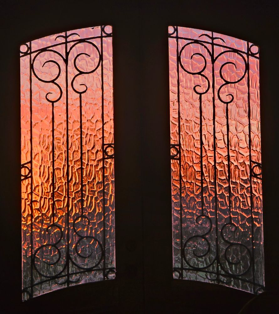 A pink and orange ombre sky seen through the frosted windows of the same wooden double door as the previous photo