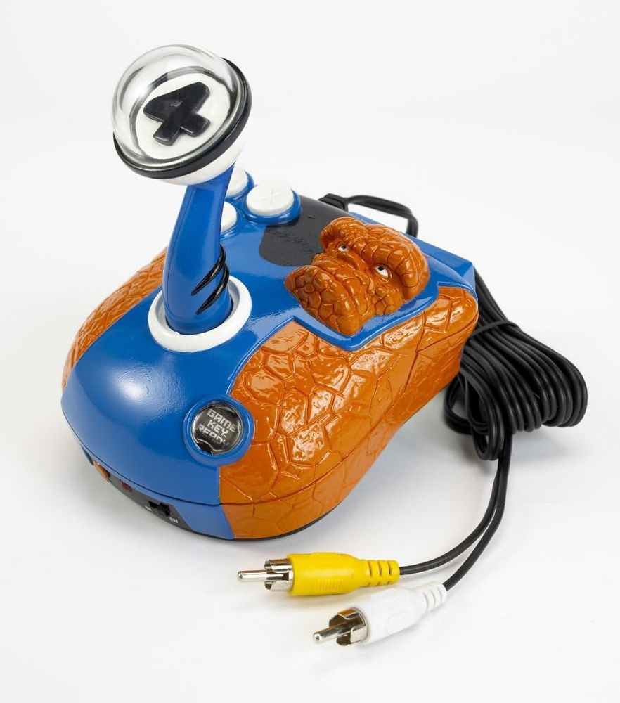 This image shows a Fantastic Four-themed TV Plug & Play video game system by JAKKS Pacific. The controller is shaped and decorated with an orange rocky texture resembling The Thing's appearance, a member of the Fantastic Four. It features a joystick with a translucent "4" symbol on top, buttons for gameplay, and AV cables for connecting to a television. This design is highly stylized to represent Marvel's Fantastic Four franchise.