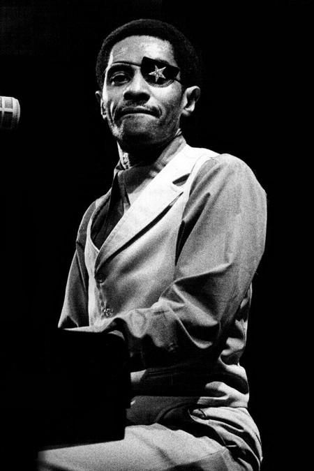 A photo of James Booker playing the piano. He is wearing an eye patch with a star on it. 