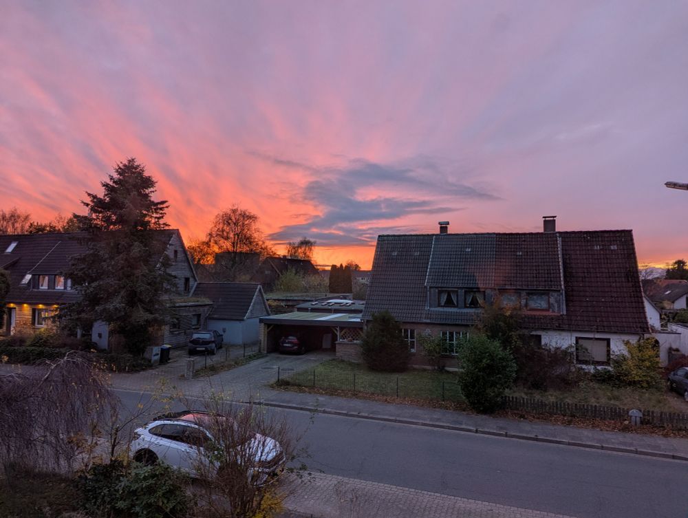 A view outside a window showing a street and a sky with gew clouds. The sun is setting and part of the sky glows in an orange color.