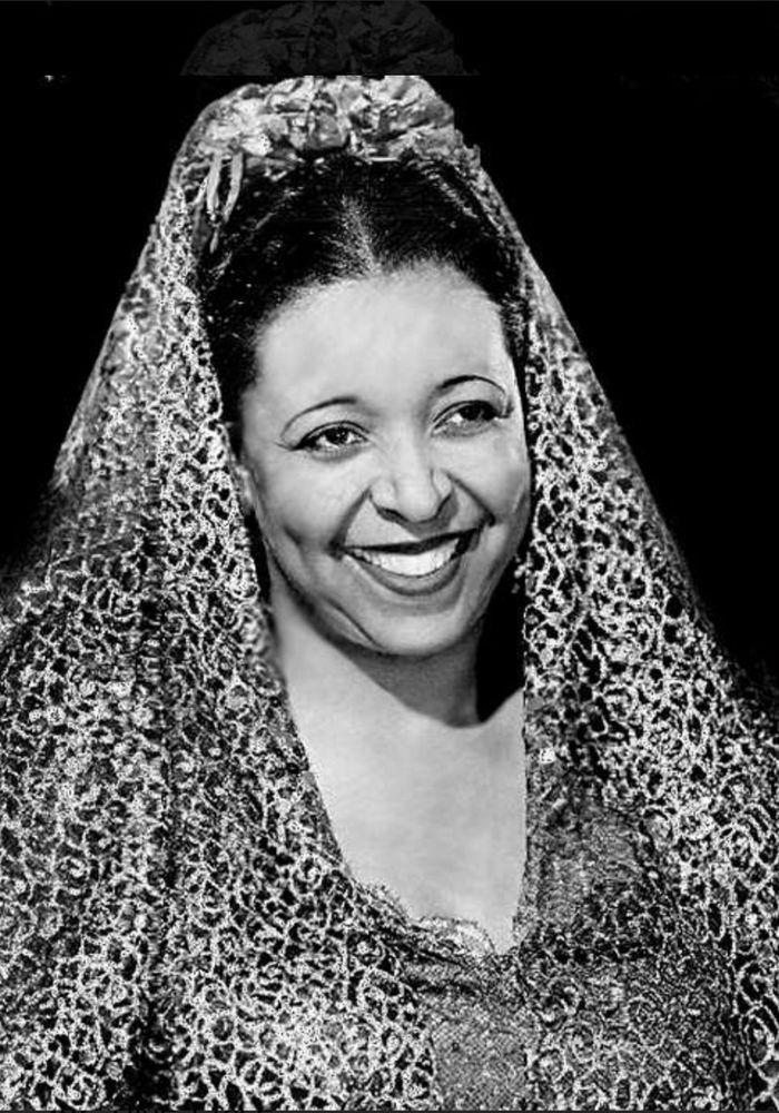 Black-and-white portrait of Ethel Waters smiling warmly, draped in a shimmering lace head covering that frames her face.