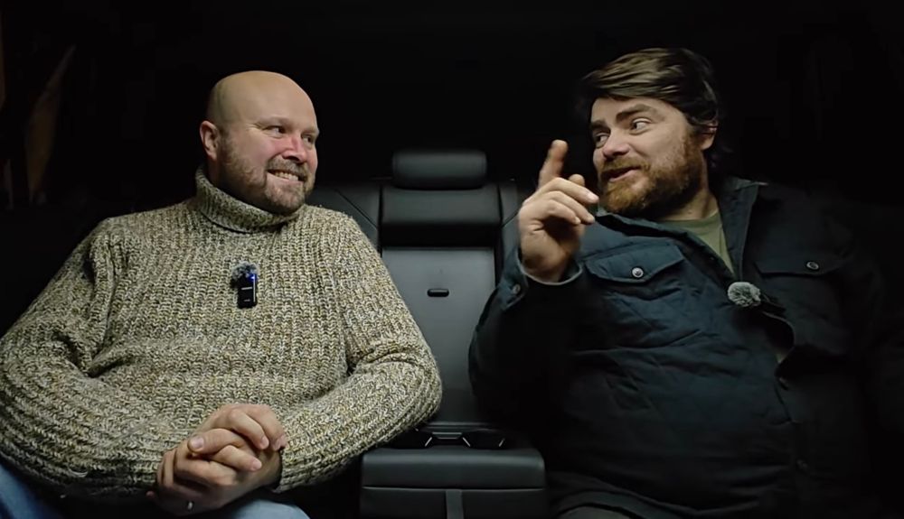 Scrof and Kitch pontificating in the back seat of a car, in darkness. Scrof is smiling while Kitch speaks, his finger held aloft to prove a point. Probably about old Citroens.