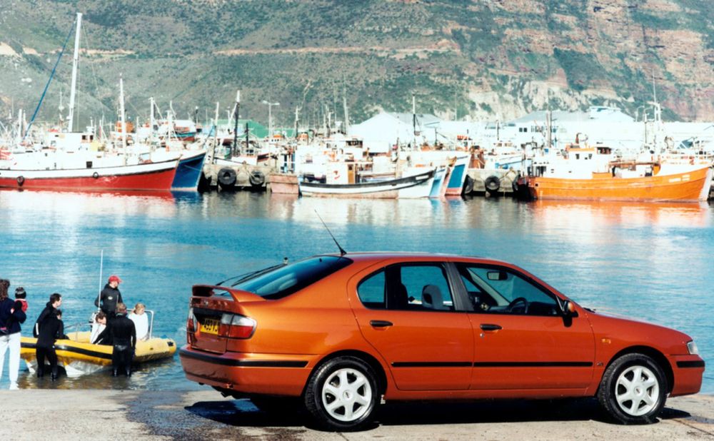 A Mk2 Nissan Primera in metallic orange, with fishing boats behind it