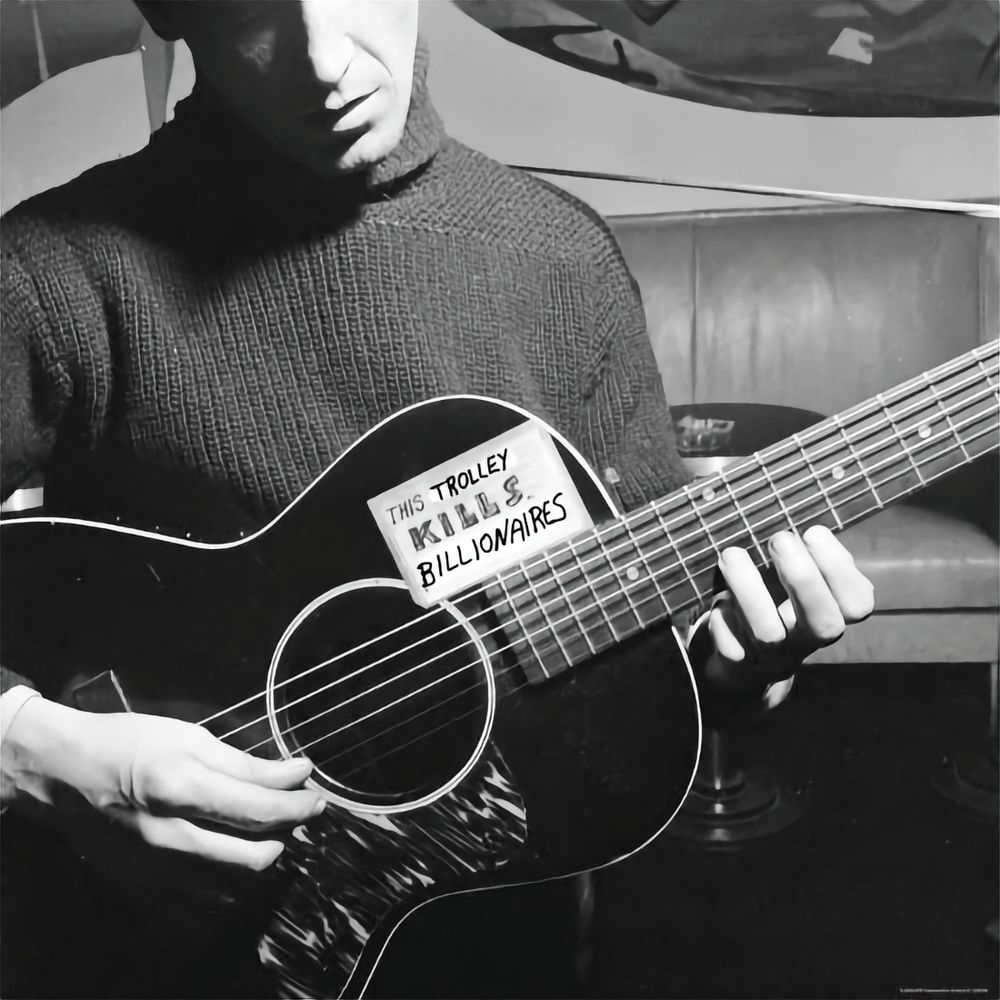Woody Guthrie, holding a guitar crudely labeled 