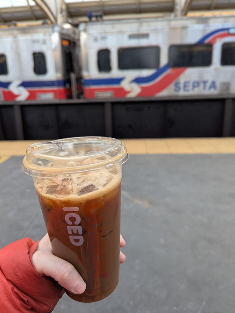 Hand holding an iced coffee with a SEPTA regional rail train in the background