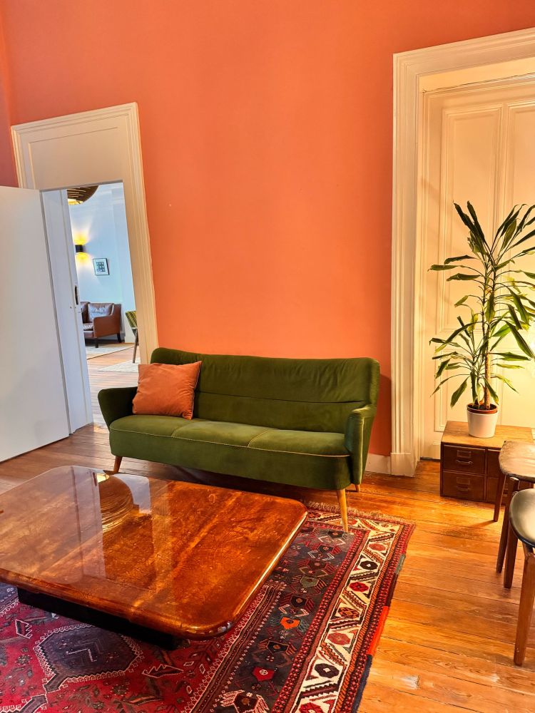 Lounge with salmon walls, Persian rug, moss green velvet couch, large shining wood coffee table, and a plant