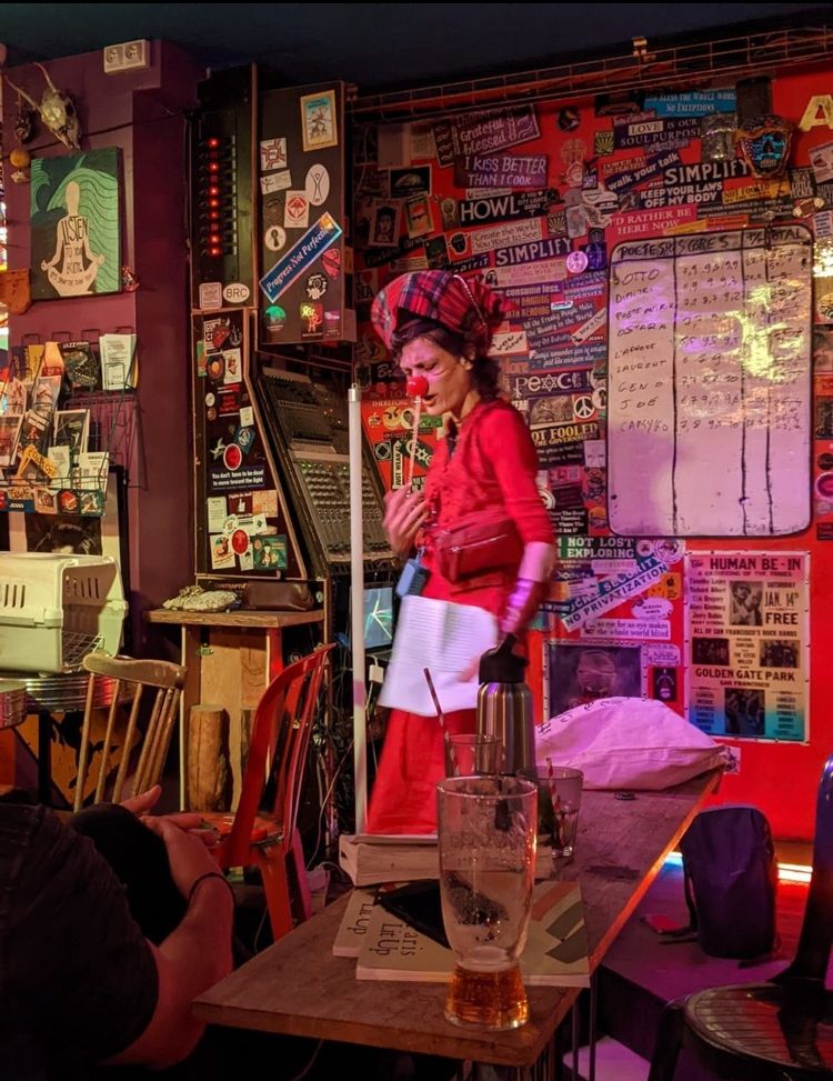 Person wearing  a red dress, colorful head gear and clown nose on stage at Paris Lit Up
