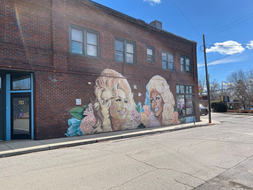 Mural of Dolly Parton and RuPaul on a brick storefront.
