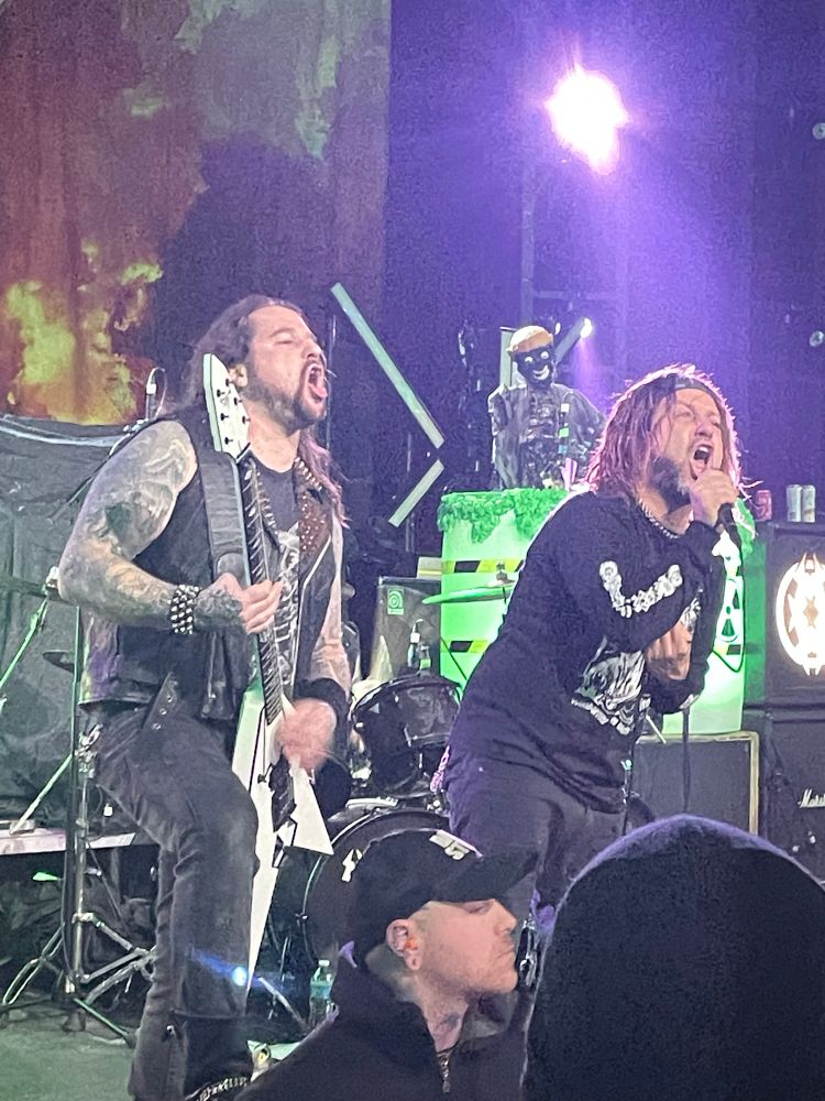 Shows a heavy metal guitarist and vocalist both making a face while singing
