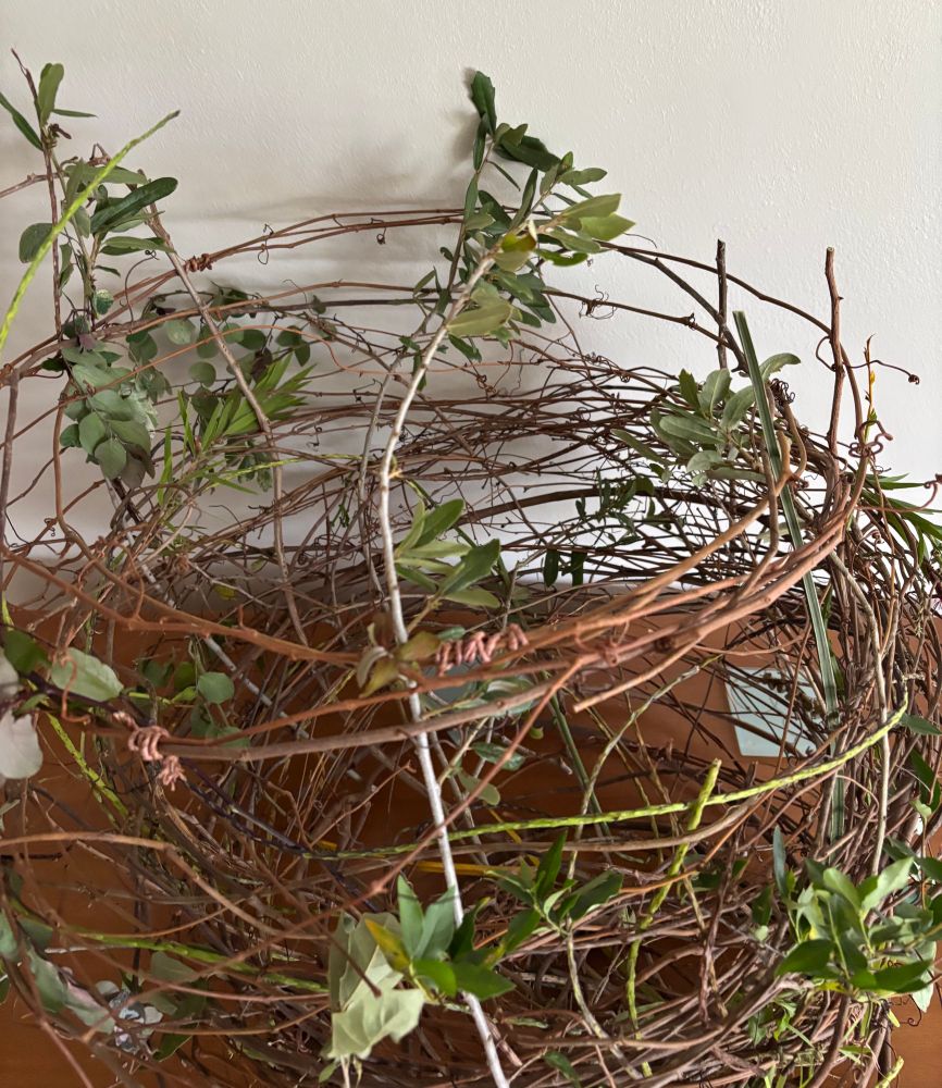 A vine and branch bird’s nest floral design. It is brown and green, open and airy.