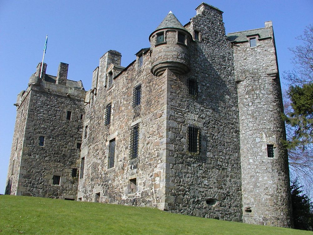 Elcho Castle, close to the south bank of the River Tay south-east of Perth. The image shows the exterior of Elcho Castle from lower down the hill on which it stands. It is four storeys in height and built of grey stone. It is externally complete and many of the windows are covered in metal grilles. The sky is blue.