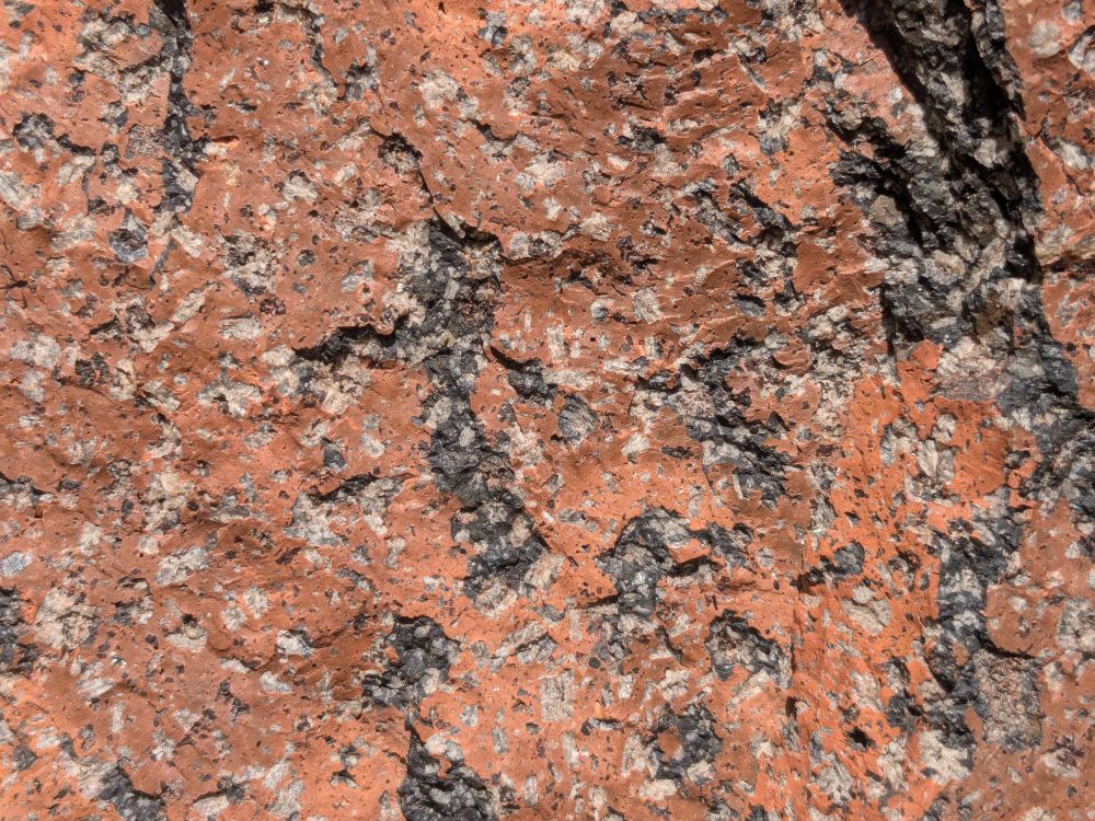 Photo of a rock with dark gray groundmass interspersed with light gray crystals of plagioclase. Across most of the rocks the groundmass has weathered to a orange-pink color, except on freshly exposed broken surfaces.