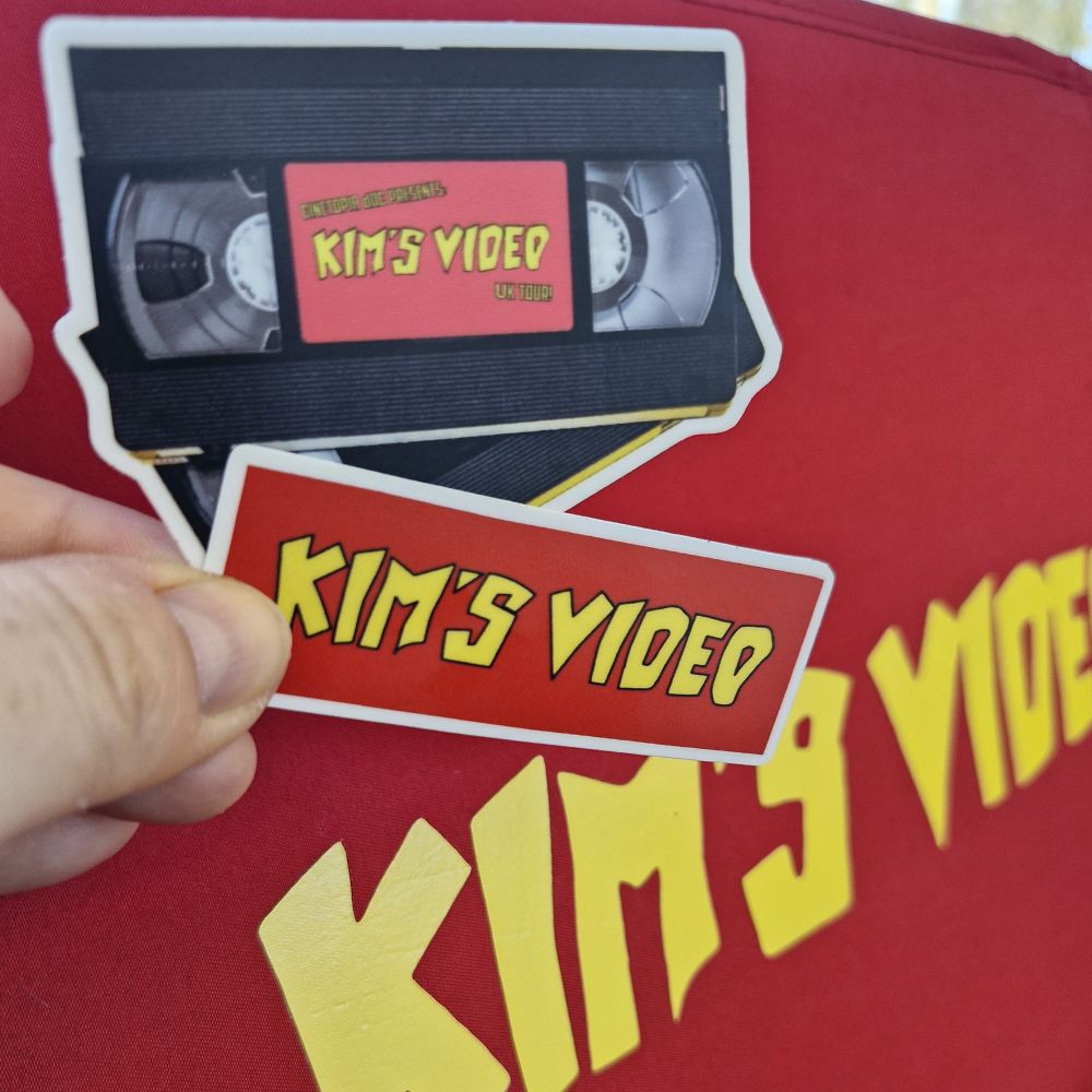White hand holding two stickers. One says Kim's Video, the other is video cassette shaped.