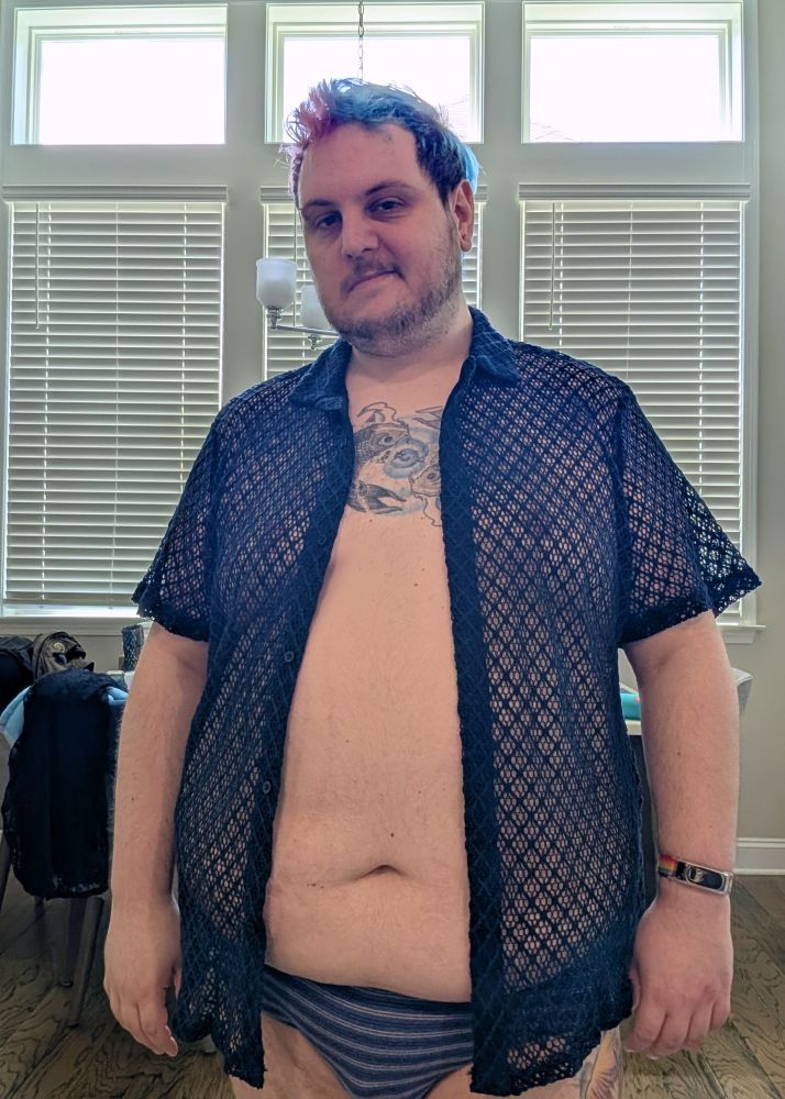 A chubby white person in a navy colored knit button down shirt. The knit has lots of gaps allowing the skin under the shirt to be visible. The shirt is open exposing their belly. They also have blue striped briefs on.