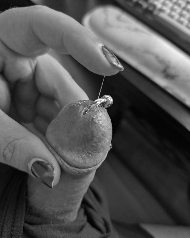 A black and white photo of a penis poking out of underwear. There's a strand of precum stretching from the head to a finger. 